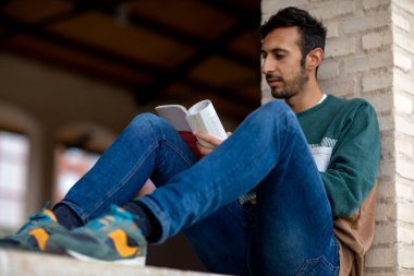 Genç Sakallı Adam, sabah vakti parkta oturmuş kitap okuyor.