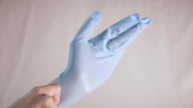 Hastanenin açık beyaz arka planında tek kullanımlık tıbbi steril mavi eldiven giymeye yakın çekim. Bir doktor ya da hemşire ellerinizi enfeksiyon ve mikroplardan korur. Yüksek kalite 4k görüntü