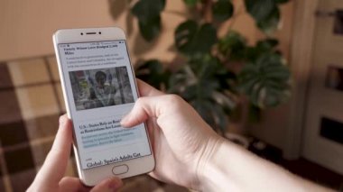 Bir kişi elinde akıllı bir telefon tutuyor ve bir koronavirüs salgını sırasında New York Times gazetesinde haberi okuyor. Video doğal gün ışığıyla çekilmiş. Yüksek kaliteli görüntüler
