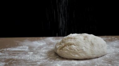 Çiğ ekmek masadaki siyah arka planda pişirmek için hazırlanır. Ekmek onu çıtır çıtır yapmak için un serpiştirilir. Bu video 4K 'de doğal ışık ile yakın plan çekilmiş.