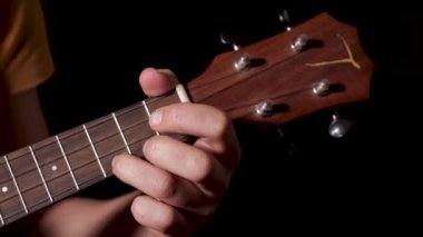 Kara ayda dört telli ukulele çalan bir müzisyenin ellerinin yakın çekimi 4K 'de yapay profesyonel ışıklandırma altında izole edilmiş bir arka plan.