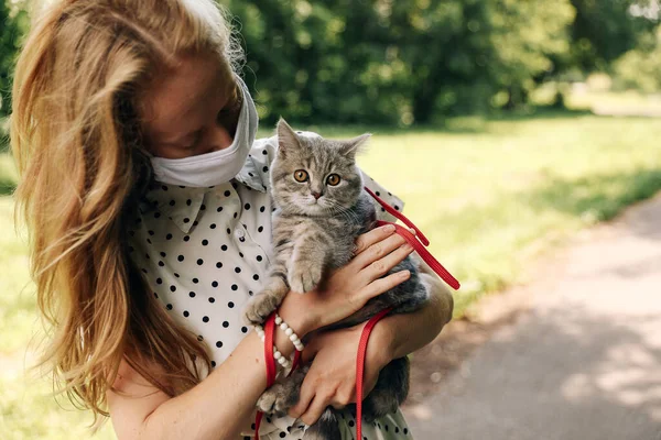 19岁的年轻金发女子戴着医疗保护面具 夏天和一只苏格兰纯正的小猫散步时 正面临着一场大流行病的感染 高质量的照片 — 图库照片