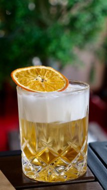 Köpüklü köpüklü ve kurutulmuş portakal dilimli kristal bardakta servis edilen klasik viski kokteylinin yakın çekimi. Serinletici alkollü içecek bar, parti ve restoran temaları için mükemmel..
