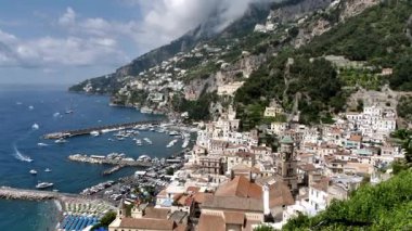 Scenic panoramic view Amalfi town on Coast, Italy. Colorful houses, church tower, marina with boats along Mediterranean Sea, surrounded by steep cliffs and green hills. Italian Riviera UNESCO World 
