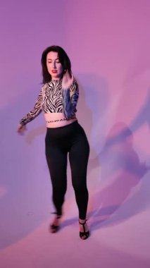 Bachata Lady Style on neon purple background lighting, Young brunette Caucasian woman dancing feminine choreography. vertical, general close-up