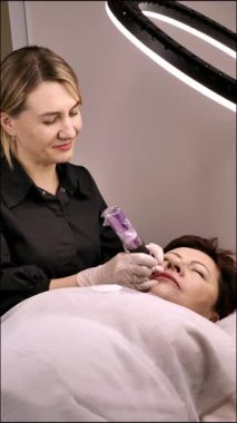 Kalıcı dudak makyajı. 50 yaşını geçmiş güzel bir kadın. Bir güzellik salonunda. Bir güzellik uzmanı yüzüne dövme yaptırıyor.. 