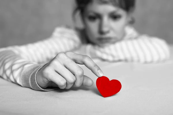 Upset and sad girl is touching red heart with finger