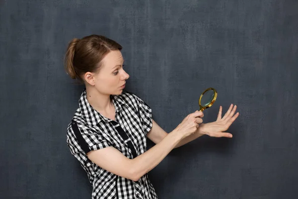 Woman is looking with surprise at her nails through magnifier