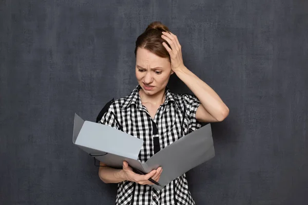 Portrait of dissatisfied woman looking at documents in folder
