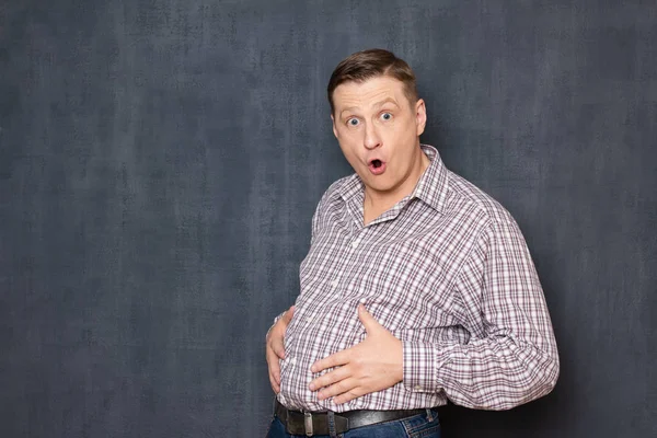 Portrait of surprised shocked man touching his big fat stomach