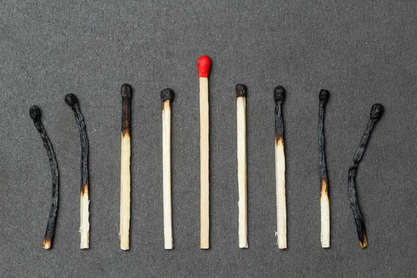 One unburned match with red head and burned matches on both sides, over gray background. Concept of leadership. Close-up shot, top view — Stock Image One Unburned Match Red Head Burned Matches Both Sides Gray Royalty Free Stock Photos