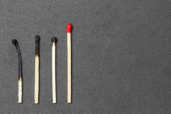 One unburned match with red head and several burned matches are placed over gray background. Concept of leadership. Close-up shot, top view — Stock Image One Unburned Match Red Head Several Burned Matches Placed Gray Stock Picture