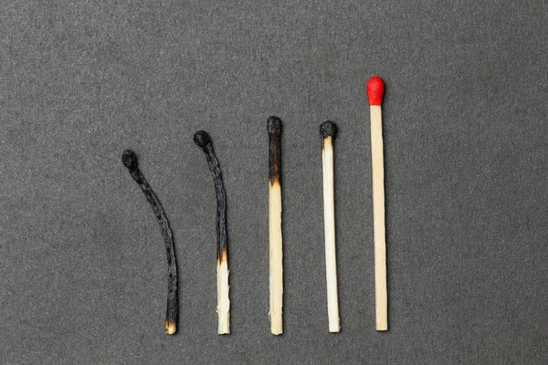 One unburned match with red head and several burned matches are placed over gray background. Concept of leadership. Close-up shot, top view — Stock Image One Unburned Match Red Head Several Burned Matches Placed Gray Stock Picture
