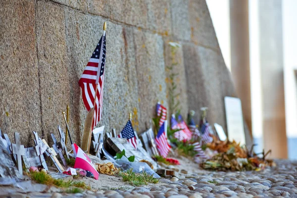 Stany Zjednoczone i kanadyjskie flagi, kwiaty i przedmioty w pamięci poległych w Normandii lądowania. Pomnik Omaha Beach. Francja. — Zdjęcie stockowe