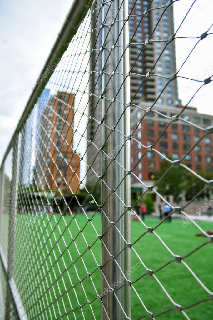 Soccer field concept out of focus in the city of NYC., Manhattan, between skyscrapers. Fence in the foreground focused.