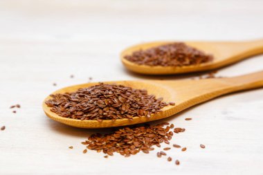 Beyaz arka planda izole edilmiş tahta kaşıklardaki keten tohumları