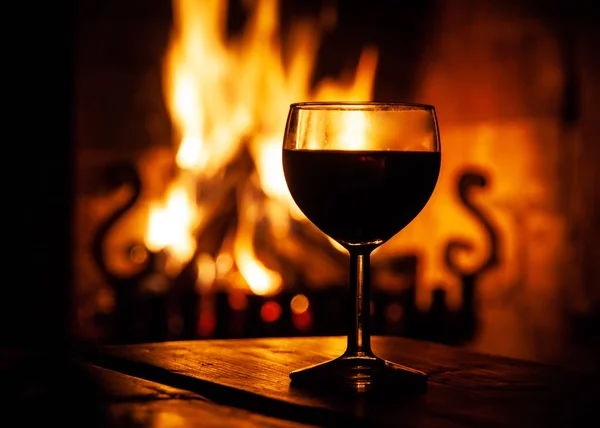 Glass of red wine on the wooden table with burning fire on the background. Evening relax on cozy place. Dark medieval style winery — Stock Photo, Image