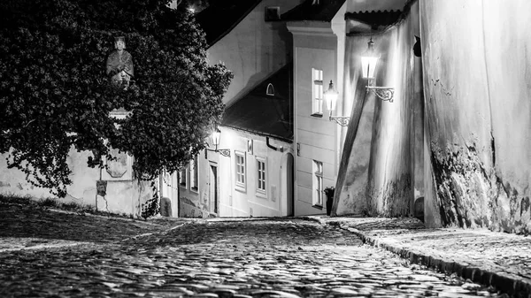 Smalle geplaveide straat in de oude middeleeuwse stad met verlichte huizen door vintage lantaarnpalen, Novy svet, Prague, Tsjechië. Nacht geschoten — Stockfoto