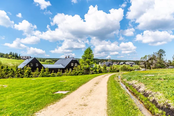 Zonnige zomerdag in Jizerka Mountain Village. Stoffige landweg, groene weiden en blauwe hemel met witte wolken, Jizera Mountains, Tsjechische Republiek — Stockfoto