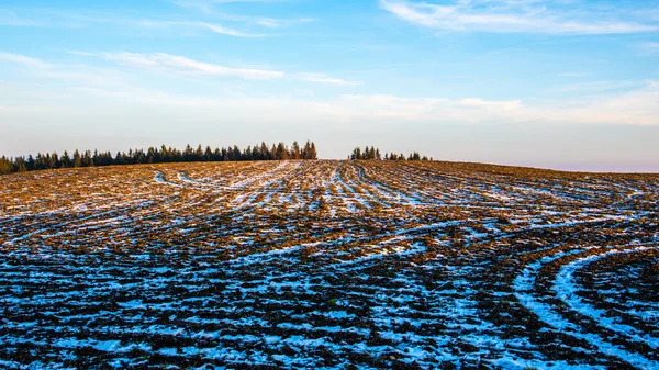 Mrożone pole orne z pozostałościami śniegu w słoneczny zimowy wieczór — Zdjęcie stockowe