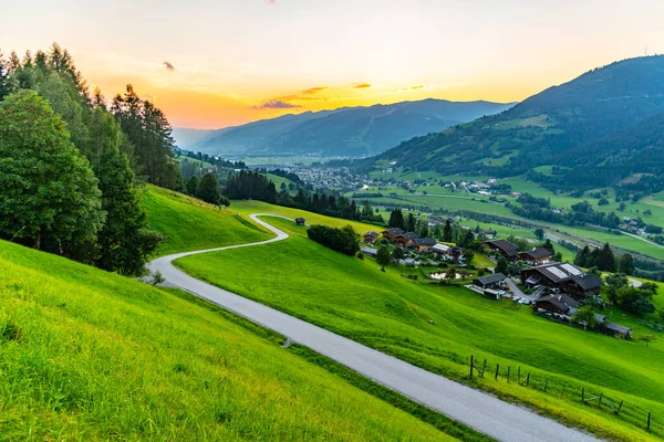 Romantic sunset in the mountains. Alpine rural curvy road, green meadows and high peaks of Austrian Alps. Pinzgau, Austria — Stock Photo, Image