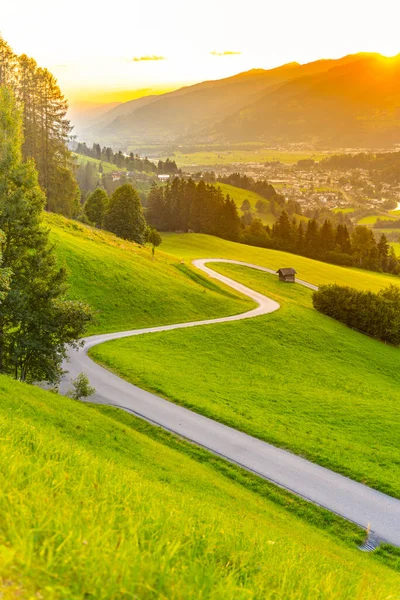 O pôr-do-sol romântico nas montanhas. Estrada curvilínea rural alpina, prados verdes e altos picos de Alpes austríacos. Pinzgau, Áustria — Fotografia de Stock