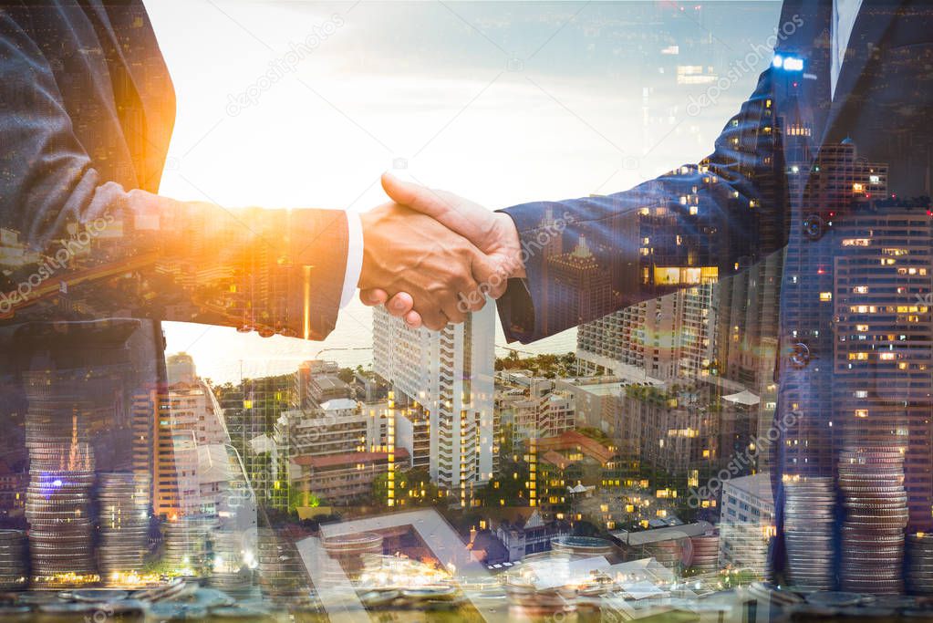 Double exposure businessmen team ,partner handshake to work agreenment about real estate .They wearing suite business uniform with blur cityscape , money and building background.