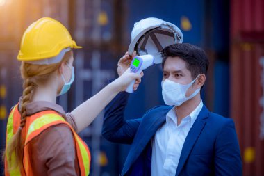 İşçi fabrikada çalışmaya başlamadan önce personel vücut ısısını ölçmek için tıbbi dijital sıcaklık termometresi kullanmış. Yüz maskesi takıyorlar..