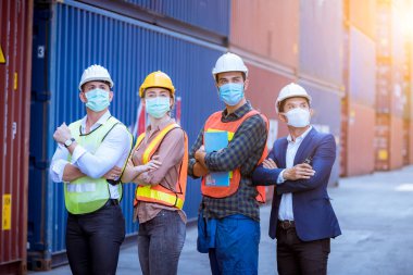 Portre ekibi rıhtım işçileri fabrikadaki kirliliği ve virüsü korumak için liman konteynırı deposunda ve güvenlik maskesi yüzünde çalışma ve kontrol altında poz veriyorlar..