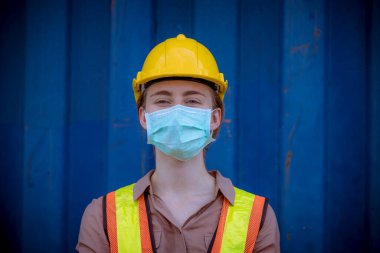 Portre kadın rıhtım işçisi, fabrikadaki kirliliği ve virüsü korumak için liman konteynır deposu ve güvenlik maskesinin üretim sürecini kontrol ediyor..