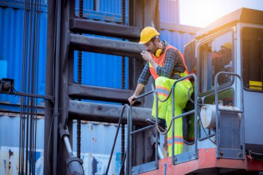 Liman işçisi, liman konteynır nakliye deposunda çalışıyor güvenlik üniforması, şapka, kulaklık takıyor ve telsiz iletişimi kuruyor..