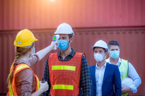 工場で働く前にスタッフの体温を確認するために医療用デジタル温度計を使用し 顔マスクを着用してコロナウイルススクリーニングの概念 — ストック写真