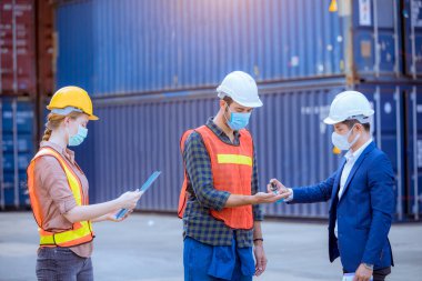 Mühendis rıhtım işçisi, virüsün virüsten ve kirlilikten korunmak için yüz maskesi takarak liman konteynırında çalışan işçi ve mühendislere bulaşan virüsü korumak için temiz ele alkol jeli sürüyor..