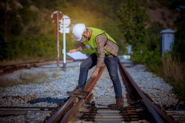 The engineer under inspection and checking construction railroad station .Engineer wearing safety uniform and safety helmet in work wearing mask for safety from virus.