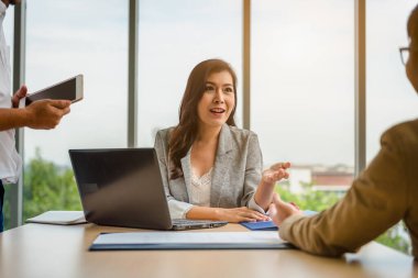 Kendine güvenen Asyalı genç bir iş kadını dizüstü bilgisayarla çalışıyor ve ofis işlerinde başarılı olmak için masadaki evrak dosyalarını kontrol ediyor..