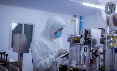 Koruyucu süit ve eldiven giyen teknisyenler, virüse karşı güvenli ve korunaklı yüz maskesi üretim sürecine sahip denetleme makineleridir.