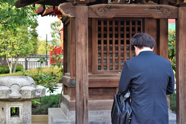An Asian man in a blue suit bows in prayer in a shrine