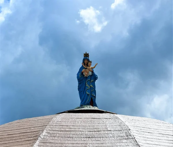 A statue of the Virgin Mother Mary carrying the baby Jesus stands on top of a white dome of a church