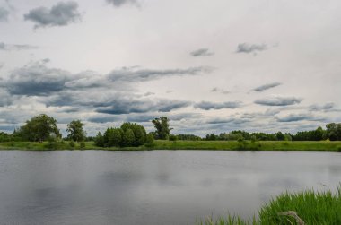 bir göl ile yeşil bir alan ve ülke yolu üzerinde manzara yağmur bulutları