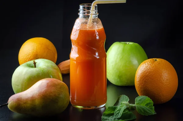 Färsk juice från apelsin grönt äpple med päron och morötter i en flaska med halm framsidan på en svart bakgrund — Stockfoto