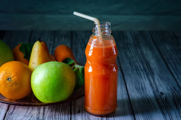 Fresh juice from orange green apple with pears and carrots in a bottle with a straw front view on wooden background — Stock Photo, Image