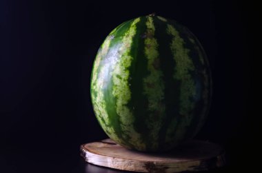 Olgun bütün karpuz siyah bir arka plan karşı ahşap bir tahta üzerinde duruyor