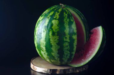 Olgun bütün karpuz siyah bir arka plan karşı ahşap bir tahta üzerinde duruyor
