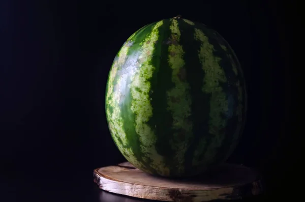 Reife ganze Wassermelone steht auf einem Holzbrett vor schwarzem Hintergrund — Stockfoto