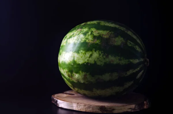 Zralý celý meloun stojí na dřevěné desce na černém pozadí — Stock fotografie