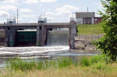 ön planda yeşil çim ve bulutlar ile mavi bir gökyüzü ile bir nehir üzerinde bir güç istasyonu eski Barajı