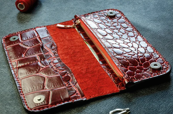 Rotes Portemonnaie für Frauen länger aus echtem Krokodilleder, handgefertigt auf dunklem Hintergrund. Nahaufnahme Stockbild