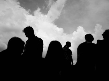 Arka planda gökyüzü olan bir grup insanın siyah beyaz silueti