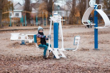 Sonbahar manzarasının arka planında şapkalı bir çocuk salıncakta sallanıyor.
