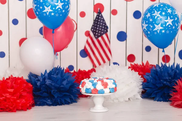 Photo zone with paper garlands, balloons, paper balls, pom poms, confetti and cream cake. Birthday cake. Smash cake. One year. Red, blue, white colors.